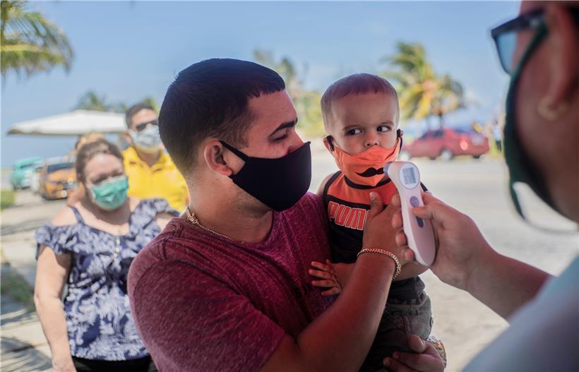 Die Polizei misst einem Kind mit Mundschutz die Temperatur an einem Kontrollpunkt am Grenzübergang zur Provinz Havanna
