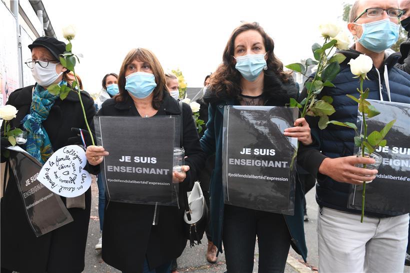 Die Teilnehmer einer Kundgebung vor einer Mittelschule halten nach einer brutalen Messerattacke Rosen und Schilder mit der Aufschrift „Ich bin Lehrer – ich verteidige die Meinungsfreiheit“. Nach der mörderischen Attacke auf einen Lehrer bei Paris sind fünf weitere Menschen festgenommen worden. Der mutmaßliche Täter war kurz nach der Tat von der Polizei getötet worden.
