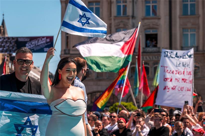 Die israelische Sängerin Yuval Raphael beim „türkisen Teppich“ am Sonntag. Im Hintergrund sind die Banner der Protestierenden zu sehen. 
