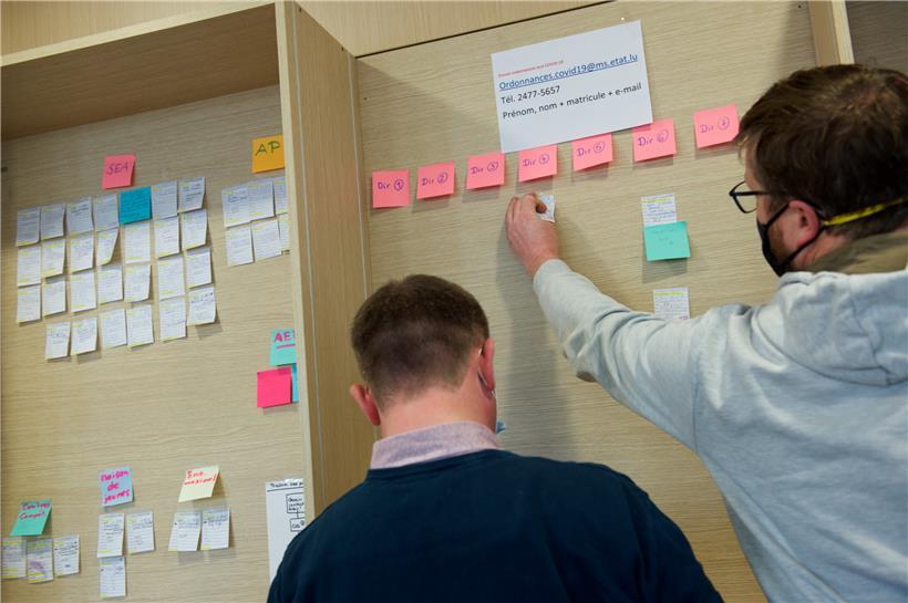 Die linke und rechte Hand von Koordinatorin Flore Schank, wie sie ihre beiden Mitarbeiter scherzhaft nennt, kleben als Backoffice des zentralen Computerordners bunte Zettelchen an eine Holzwand
