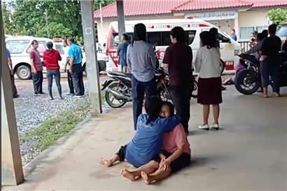 Dieses Videostandbild zeigt eine Frau, die vor dem Tatort eines Angriffs auf eine Kindertagesstätte auf dem Boden sitzt und eine andere Person umarmt. Ein ehemaliger Polizeibeamter hat in einer Kindertagesstätte in Thailand ein Blutbad angerichtet und mehr als 30 Menschen getötet. 
