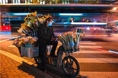 Ein Blumenverkäufer wartet auf einer Straße im Jing’an-Viertel in Schanghai auf Kunden
