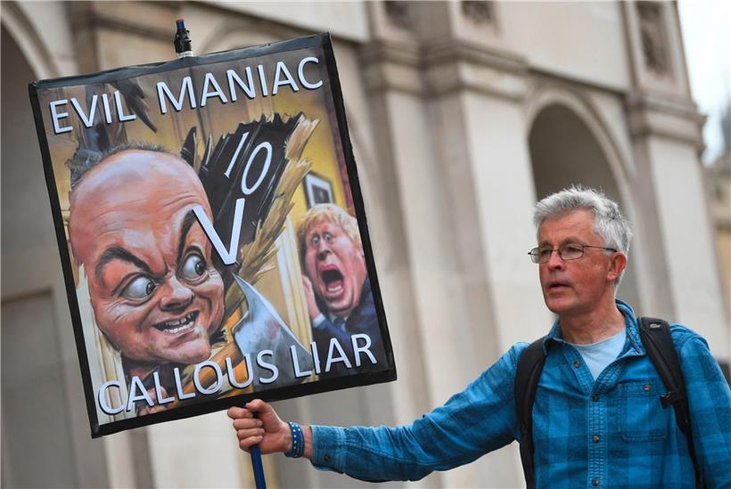 Ein Demonstrant hält vor dem britischen Parlament eine Karikatur mit dem umstrittenen ehemaligen Premier-Berater Dominic Cummings und Boris Johnson in der Hand
