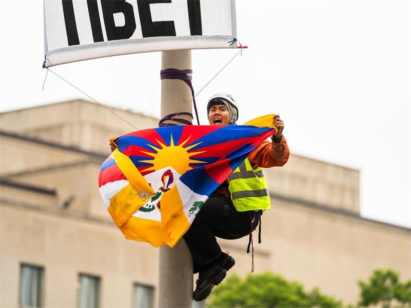 Ein Demonstrant klettert auf einen Laternenpfahl und entrollt ein Transparent, um gegen den bevorstehenden Staatsbesuch des chinesischen Präsidenten Xi zu protestieren