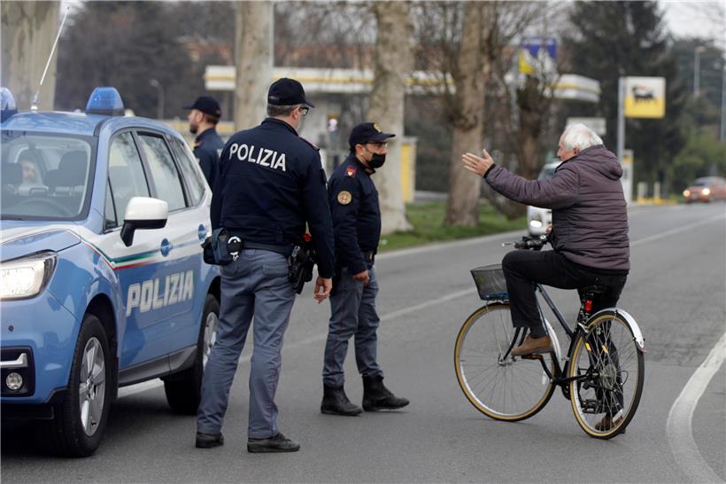 Ein Fahrradfahrer spricht mit Polizisten, die eine Straße kontrollieren, welche in ein abgeriegeltes Gebiet führt. Mit drastischen Maßnahmen wie Sperrzonen will Italien die rasante Ausbreitung des Coronavirus stoppen.
