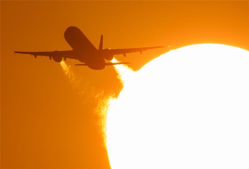 Ein Flugzeug startet vom Flughafen Frankfurt und fliegt dabei an der untergehenden Sonne vorbei
