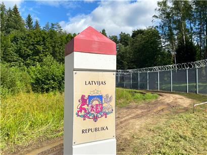Grenzpfeiler mit Aufschrift „Republik Lettland“ an der lettisch-russischen Grenze in bewaldeter Landschaft