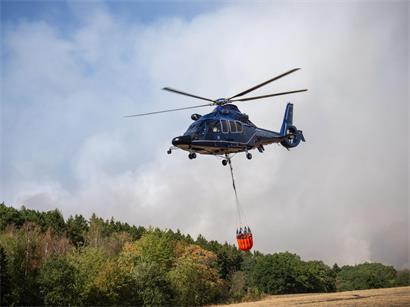 Ein Helikopter der Bundespolizei mit einem Löschwasser-Außenlastbehälter ist beim Waldbrand im Hürtgenwald im Einsatz