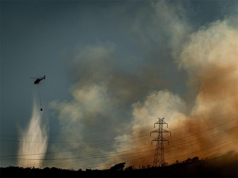 Ein Hubschrauber wirft Wasser auf einen Waldbrand ab, der im Collserola-Gebirge bei Barcelona wütet, während dichter Rauch über den Hügeln aufsteigt