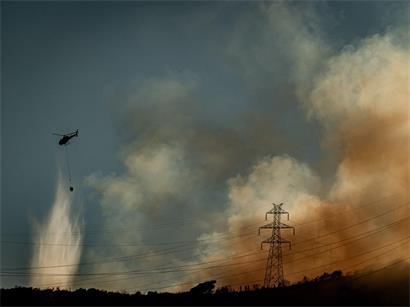 Ein Hubschrauber wirft Wasser auf einen Waldbrand ab, der im Collserola-Gebirge bei Barcelona wütet, während dichter Rauch über den Hügeln aufsteigt