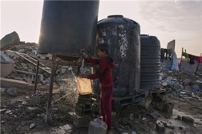 Ein Jugendlicher holt Wasser aus einem Tank neben den Trümmern von Gebäuden, die bei israelischen Luft- und Bodenoperationen zerstört wurden
