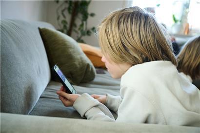 Ein Junge liegt auf einem Sofa und guckt auf sein Smartphone
