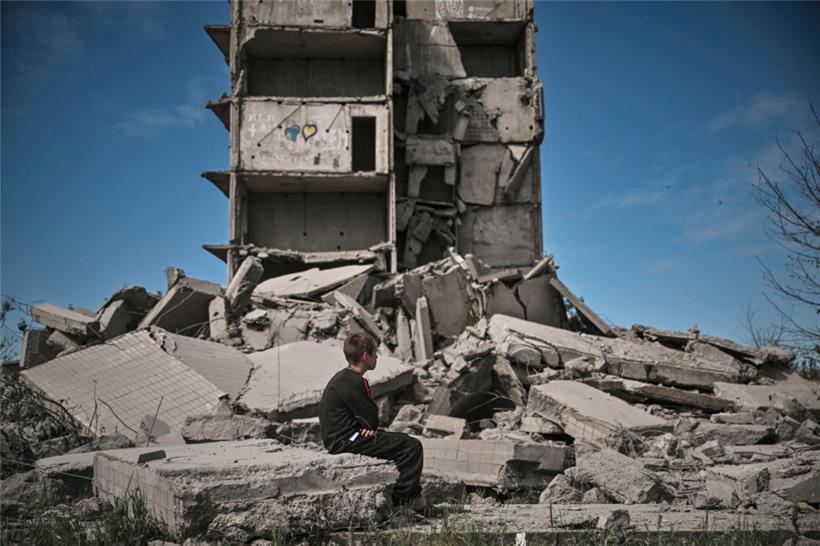 Ein Junge sitzt in Kramatorsk im Donbass vor einem zerstörten Gebäude
