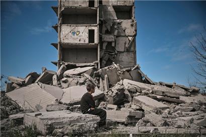 Ein Junge sitzt in Kramatorsk im Donbass vor einem zerstörten Gebäude
