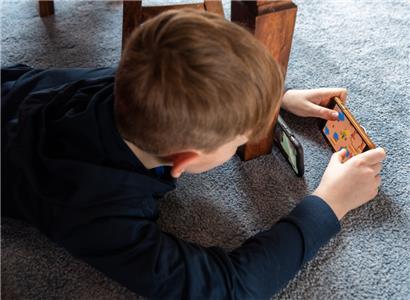 Ein Junge spielt ein Videospiel auf seinem Smartphone und überträgt es mit einem zweiten Handy per Facetime zu seinem Freund
