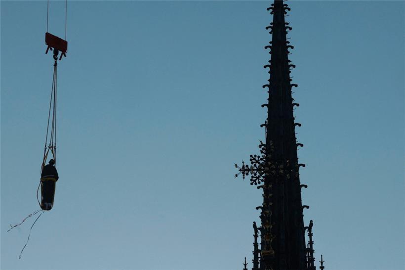Ein Kran hebt eine der 16 riesigen kupferbeschichteten Apostelstatuen an, die am 23. Juni 2025 wieder auf der Turmspitze der Kathedrale Notre-Dame de Paris in Paris aufgestellt werden
