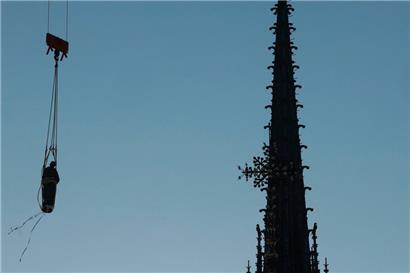 Ein Kran hebt eine der 16 riesigen kupferbeschichteten Apostelstatuen an, die am 23. Juni 2025 wieder auf der Turmspitze der Kathedrale Notre-Dame de Paris in Paris aufgestellt werden
