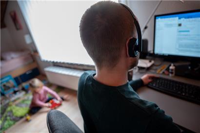 Ein Mann arbeitet im Homeoffice, während im Hintergrund sein Kind spielt
