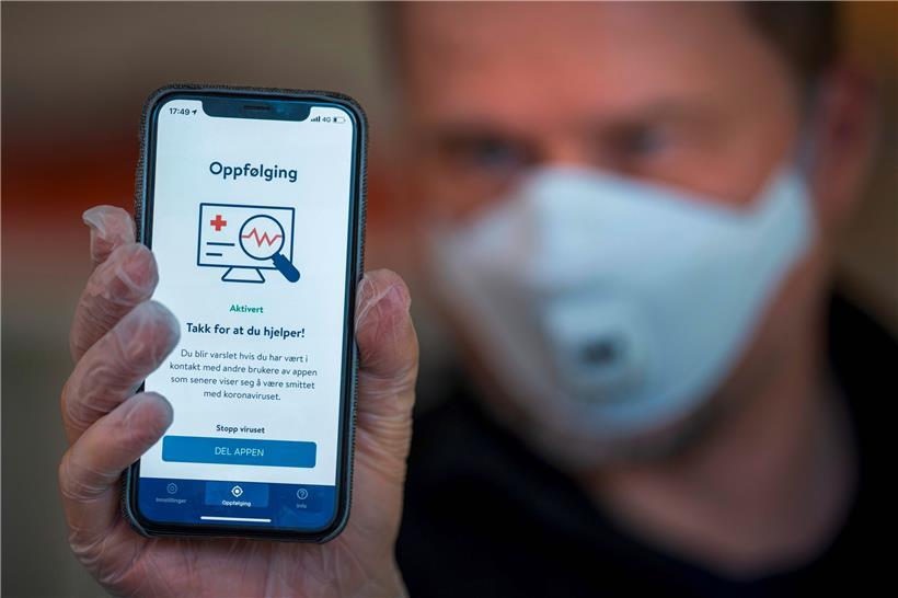 Ein Mann aus Norwegen hält ein Smartphone mit einer Tracing-App hoch. In Luxemburg ist man immer noch unentschieden, ob man die Technik einsetzen soll. 
