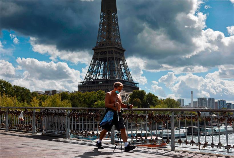 Ein Mann betreibt auf einer Brücke mit Blick auf den Eiffelturm Nordic Walking und trägt dabei einen Mundschutz.
