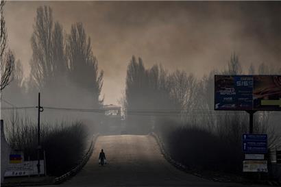 Ein Mann geht am Donnerstag über eine Brücke in der ukrainischen Hauptstadt Kiew, während Rauch aufsteigt, nachdem ein Lagerhaus nach einem russischen Bombardement am Stadtrand von Kiew zerstört wurde
