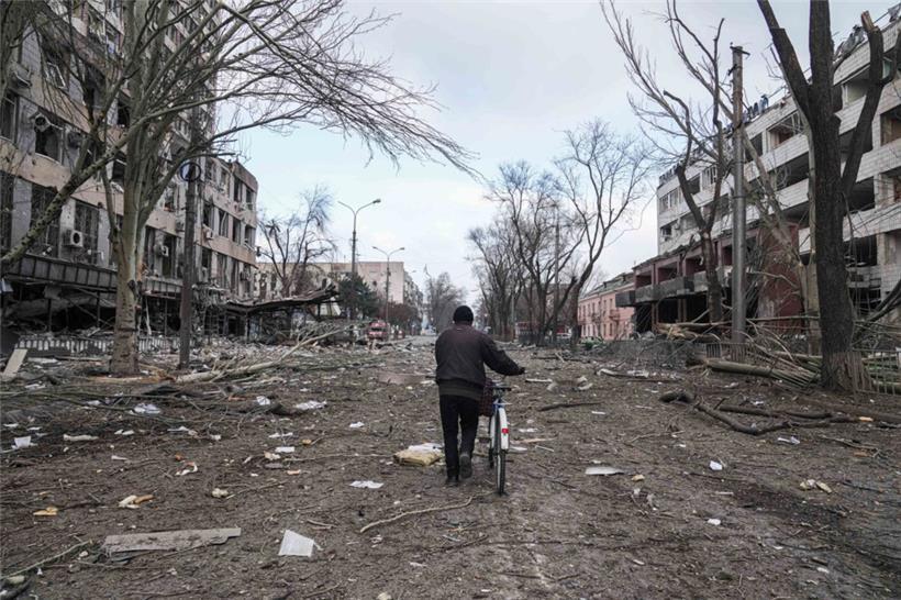 Ein Mann geht mit einem Fahrrad auf einer Straße in Mariupol, die durch einen Beschuss beschädigt wurde
