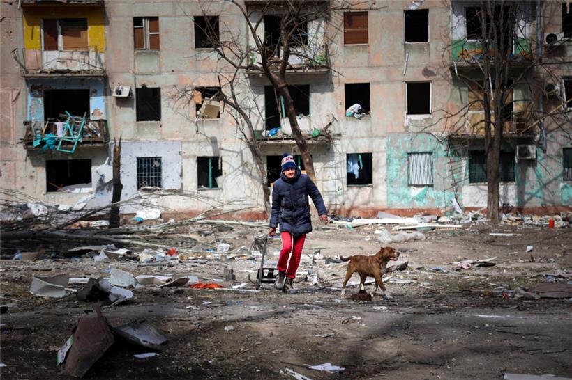 Ein Mann geht mit seinem Hund in der Nähe eines Wohnhauses entlang, das durch den Beschuss von Kämpfen am Stadtrand von Mariupol in der Ukraine beschädigt wurde
