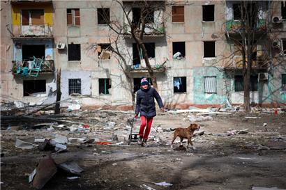 Ein Mann geht mit seinem Hund in der Nähe eines Wohnhauses entlang, das durch den Beschuss von Kämpfen am Stadtrand von Mariupol in der Ukraine beschädigt wurde
