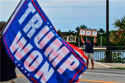 Ein Mann hält ein Schild mit der Aufschrift „Sperrt ihn ein“, während sich Anhänger des ehemaligen US-Präsidenten und republikanischen Präsidentschaftskandidaten Donald Trump in der Nähe seiner Residenz in Mar-a-Lago versammeln
