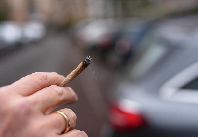 Ein Mann hält einen Joint auf einer Straße
