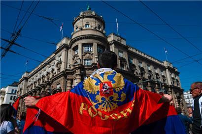 Ein Mann hält während eines Protestes vor einem Regierungsgebäude in Belgrad am 24. März gegen die EU-Pläne, eine Annäherung zwischen Serbien und dem Kosovo herbeizuführen, eine russische und eine serbische Flagge in den Händen
