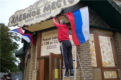 Ein Mann hängt am Dienstag eine russische Fahne an einem Café im ukrainischen Luhansk auf
