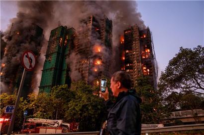 Ein Mann nimmt mit seinem Handy Rauch und Flammen auf, als ein Großbrand mehrere Wohngebäude im Wang Fuk Court in Hongkong erfasst
