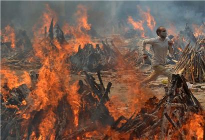 Ein Mann rennt, um der Hitze zu entkommen, die von den mehreren Holzfeuern mit Covid-19-Opfern in einem Krematorium in den Außenbezirken von Neu-Delhi ausgeht
