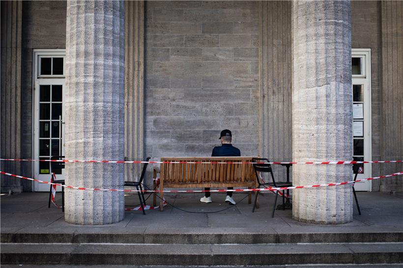 Ein Mann sitzt auf einer mit rot-weißem Absperrband gesicherten Bank vor einem Kaffee in der Innenstadt. Gut einen Monat nach dem Shutdown bereitet sich Hamburg auf eine erste Lockerung der Corona-Auflagen vor. Grundsätzlich werden die Kontaktbeschränkungen aber bis mindestens zum 3. Mai verlängert.
