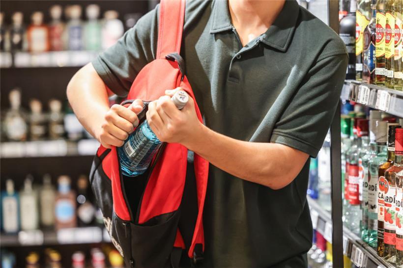 Ein Mann steckt in einem Supermarkt eine Flasche mit einem alkoholhaltigen Getränk in seinen Rucksack. (Illustration) 
