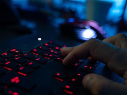 Mann im dunklen Raum tippt konzentriert auf beleuchteter Tastatur – Arbeiten im Homeoffice bei Nacht