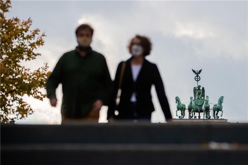 Ein Mann und eine Frau mit Mund-Nasen-Schutz gehen vor der Quadriga des Brandenburger Tores.

