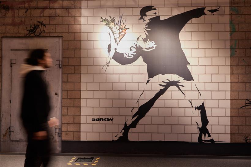 Ein Mitarbeiter betrachtet in der Ausstellung „The Mystery of Banksy – A Genius Mind“ in der ehemaligen Galeria Kaufhof das Wandbild mit dem Titel „Flower Thrower“
