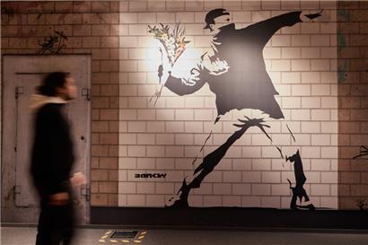 Ein Mitarbeiter betrachtet in der Ausstellung „The Mystery of Banksy – A Genius Mind“ in der ehemaligen Galeria Kaufhof das Wandbild mit dem Titel „Flower Thrower“
