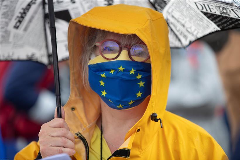 Ein Mitglied einer pro-europäischen deutschen Vereinigung steht mit Regenschirm und einer Stoffmaske im Design der Europäischen Fahne auf der „Passerelle des Deux-Rives“ (Fußgängerbrücke der beiden Ufer), die das französische Straßburg mit dem deutschen Ort Kehl (Baden-Württemberg) verbindet. 
