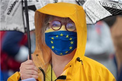 Ein Mitglied einer pro-europäischen deutschen Vereinigung steht mit Regenschirm und einer Stoffmaske im Design der Europäischen Fahne auf der „Passerelle des Deux-Rives“ (Fußgängerbrücke der beiden Ufer), die das französische Straßburg mit dem deutschen Ort Kehl (Baden-Württemberg) verbindet. 
