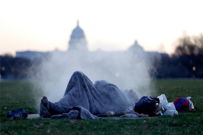 Ein Obdachloser wärmt sich auf einem dampfenden Schacht auf der National Mall auf dem Capitol Hill auf
