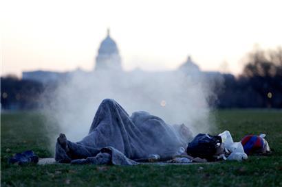 Ein Obdachloser wärmt sich auf einem dampfenden Schacht auf der National Mall auf dem Capitol Hill auf
