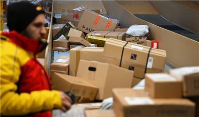 Ein Paketbote holt in einer Zustellbasis von DHL Pakete von einer Rutsche, um sie in seinen Transporter zu laden und seine Zustelltour zu beginnen

