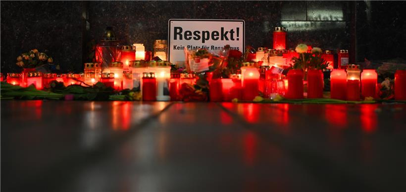 Ein Schild mit der Aufschrift "Respekt" spiegelt sich zusammen mit niedergelegten Kerzen in der nassen Straße am Tatort Heumarkt. Bei einem rassistischen Anschlag hatte ein 43-jähriger Deutscher im hessischen Hanau mehrere Menschen und sich selbst erschossen.
