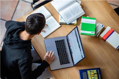 Ein Student organisiert sein Studium vom Wohnzimmer der Eltern aus und blickt auf die Webseite
