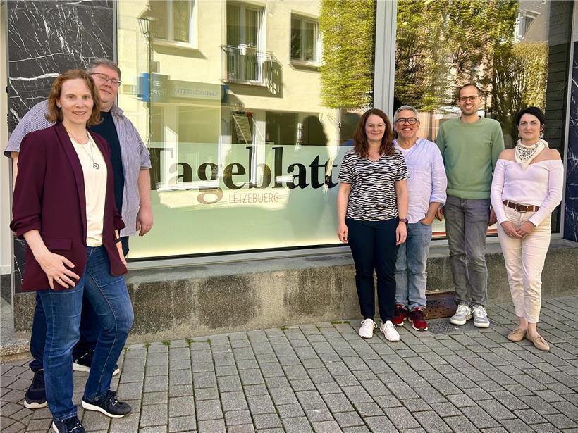 Teamfoto der Belegschaft vor moderner Agentur in belebter Fußgängerzone, Firmenstandort urban und einladend