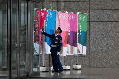 Ein Wachmann richtet ein Transparent eines Aufstellers für die Olympischen Spiele von Tokio 2020. 
