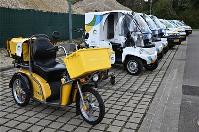 Ein älteres Elektro-Dreirad steht neben dem neuen elektrischen Zustellfahrzeug, dem Paxster
